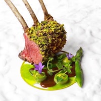 a lamb chop with asparagus and pistachios on a plate