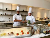 two chefs standing in front of a counter with food